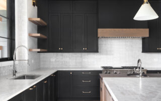 A luxury kitchen with black cabinets, granite counter top, tiled backsplash, stainless steel appliances, and chrome faucets.